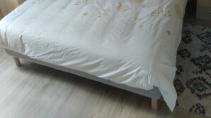 Un dormitorio con cabecera de madera, una cama con ropa de cama blanca y almohadas amarillas, una mesita de noche y una estantería de pared.