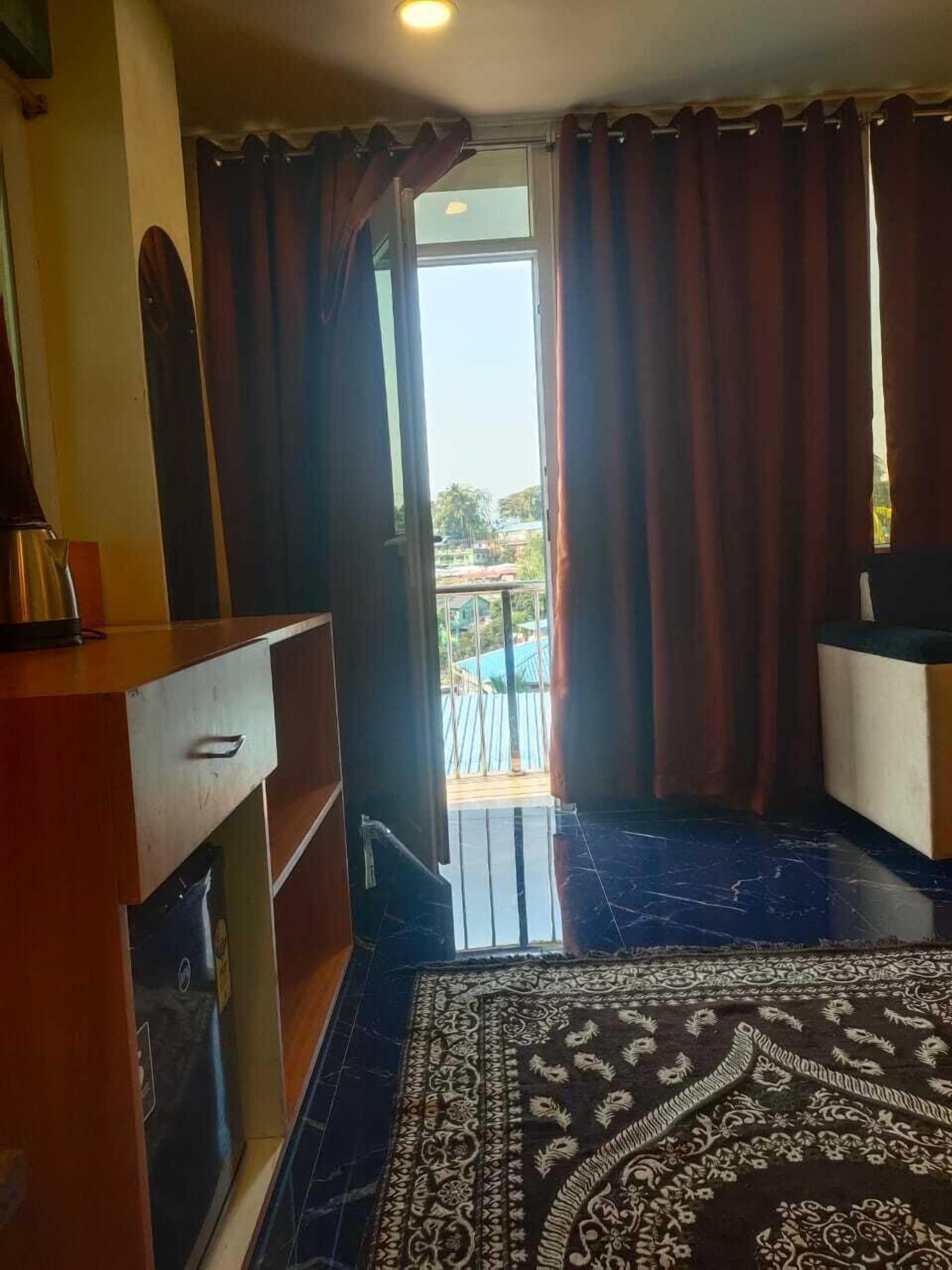 A hotel room with a bed, a desk, a chair, a window with curtains, and a view of the outside.