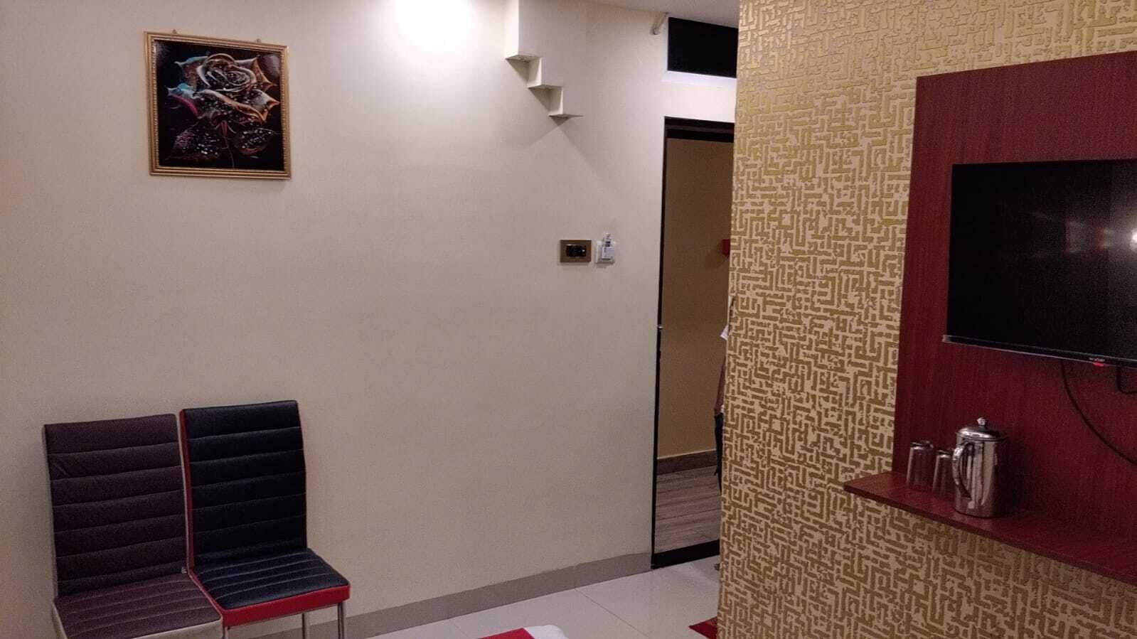 A hallway with a cushioned bench, a framed artwork on the wall, a television on a red shelf, and a patterned wall.