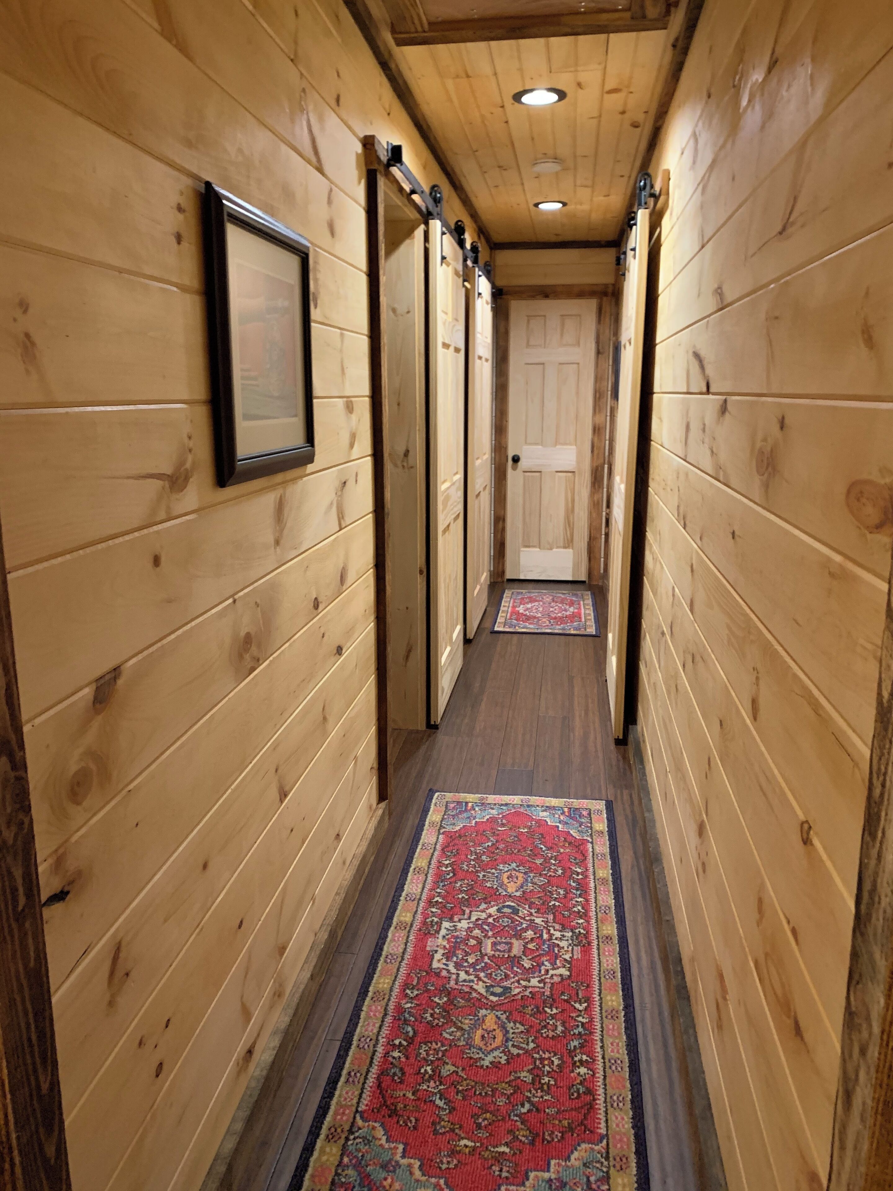 A wooden hallway with a patterned rug, wooden walls, and a door at the end.