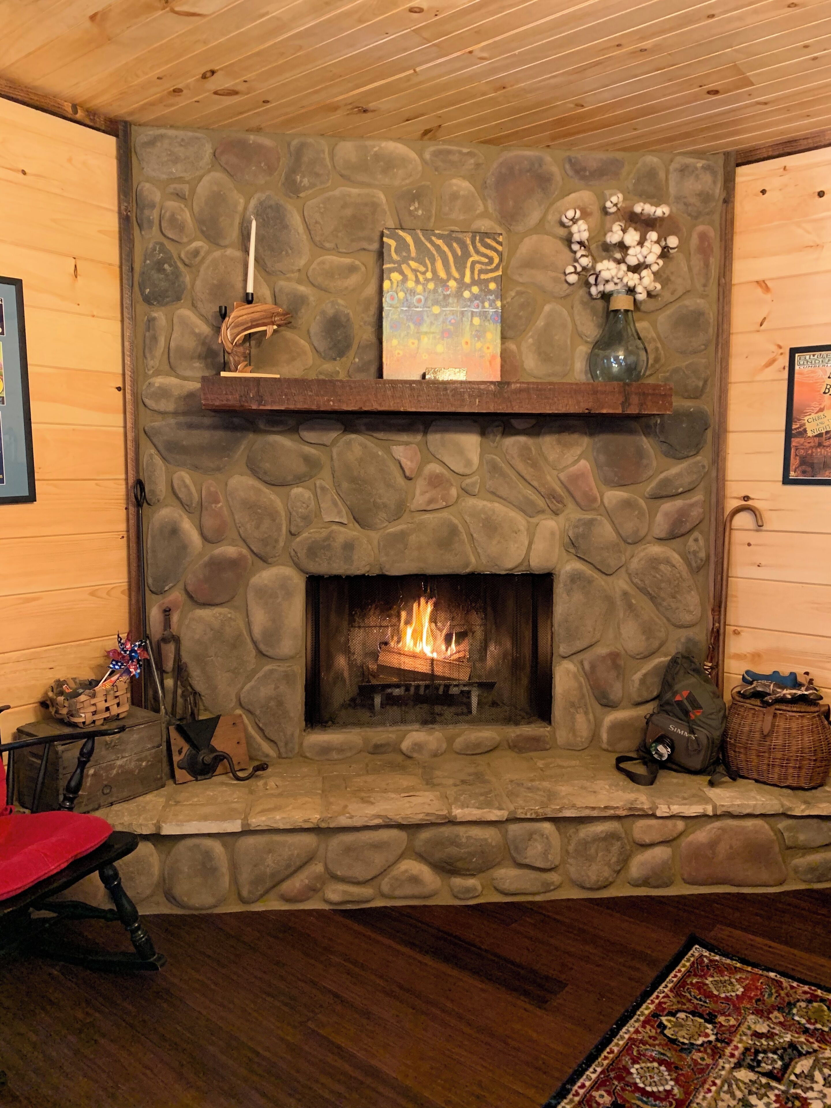 A stone fireplace with a fire, a wooden mantel, and a framed artwork above it.