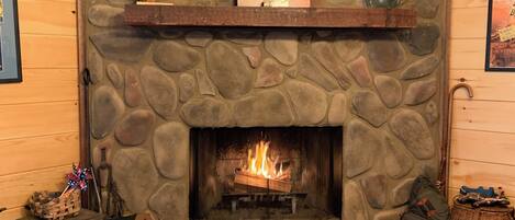 A stone fireplace with a fire, a wooden mantel, and a framed artwork above it.