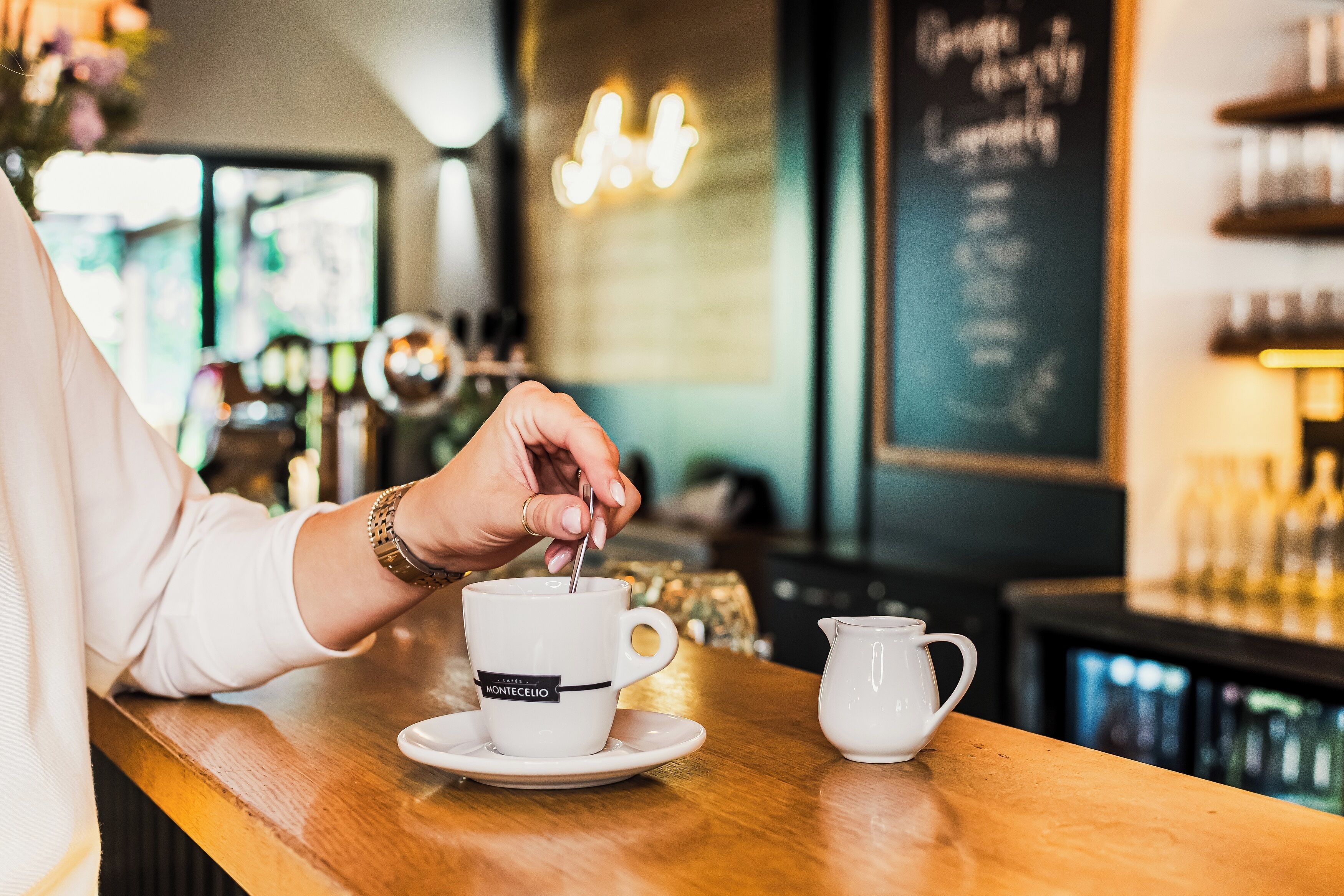 A person stirring a drink in a cup labeled "MONTECELI" at a bar.
