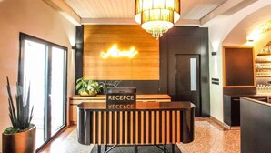 A reception desk with a sign reading "RECEPTION" and "RECEIVE" in two languages, a chandelier, wooden paneling, and a plant. - Hotel Mariel Znojmo (Znojmo)