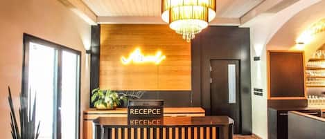 Una recepción con un cartel bilingüe, un candelabro y una pared de madera con un letrero de neón.