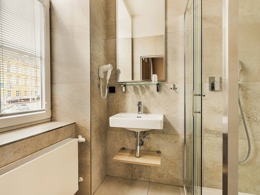 A modern bathroom with a glass shower enclosure, a white sink with a mirror above it, and a hairdryer on the wall.