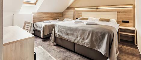 A modern, compact bedroom with two beds, a skylight, and a built-in bedside table.