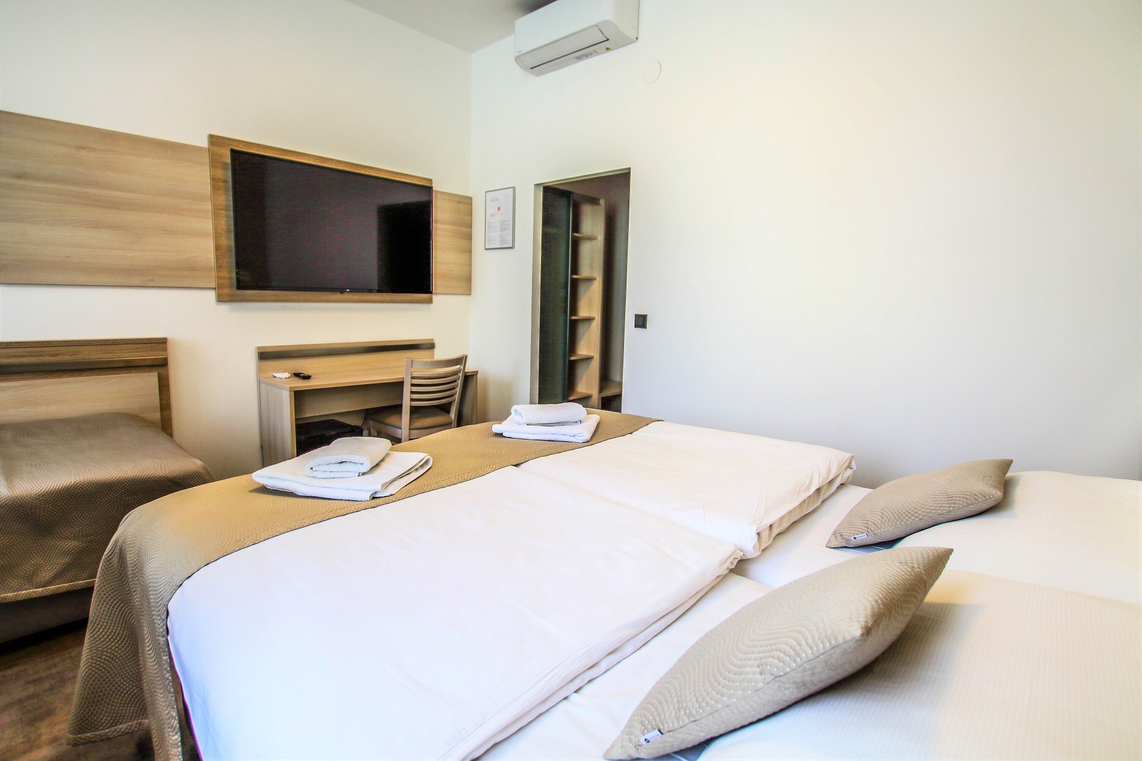 Ein Hotelzimmer mit zwei Betten, einem Fernseher, einem Schreibtisch und einem Kleiderschrank.