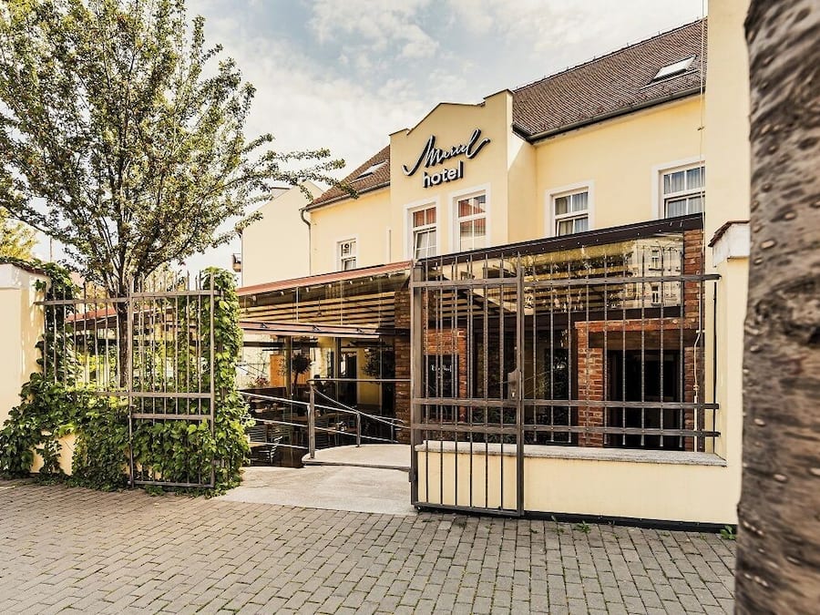 A hotel with a yellow facade, a gated entrance, and a covered outdoor seating area.