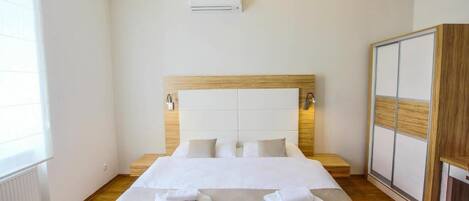 Habitación de hotel con una cama grande, cabecero de madera, armario y un equipo de aire acondicionado en la pared.