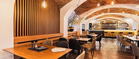 Un restaurante con mesas y sillas de madera, un muro de ladrillo y luces colgantes.