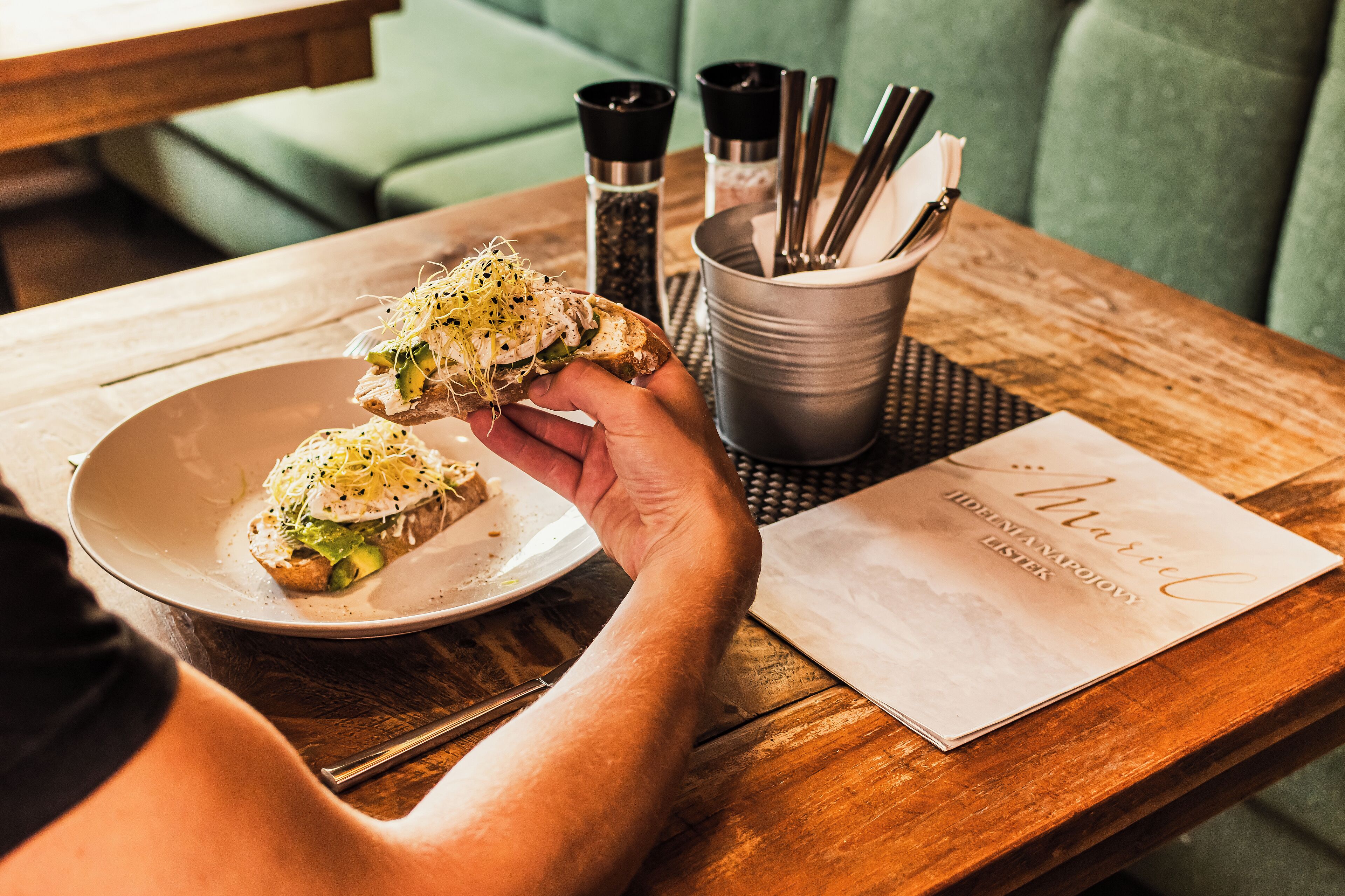 A person holding a plate with food, a menu, and a salt and pepper shaker on a wooden table.