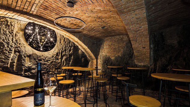 A rustic interior with stone walls, wooden tables, and a circular skylight. - Hotel Mariel Znojmo (Znojmo)