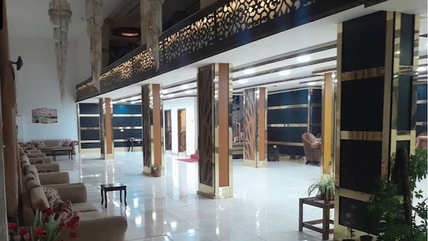 Een ruime lobby met een hoge plafond, grote pilaren en een zithoek met banken.