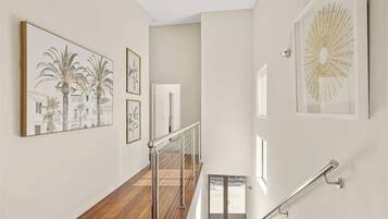 A staircase with a metal railing, a door at the top, and wall art including a palm tree painting and a sunburst design.