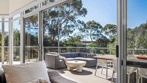 Et moderne udeområde med glasgelænder, en modulopstillet sofa, et rundt sofabord og et spiseområde med stole.