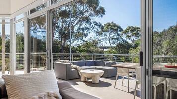 A modern outdoor living space with a glass balustrade, a sectional sofa, a round coffee table, and a dining area with chairs.