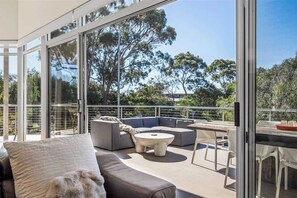 Un espace de vie extérieur moderne doté d’une balustrade en verre, d’un canapé d’angle, d’une table basse ronde et d’un coin repas avec des chaises.