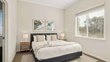 A bedroom with a bed, two bedside tables, a ceiling fan, and a window with blinds.