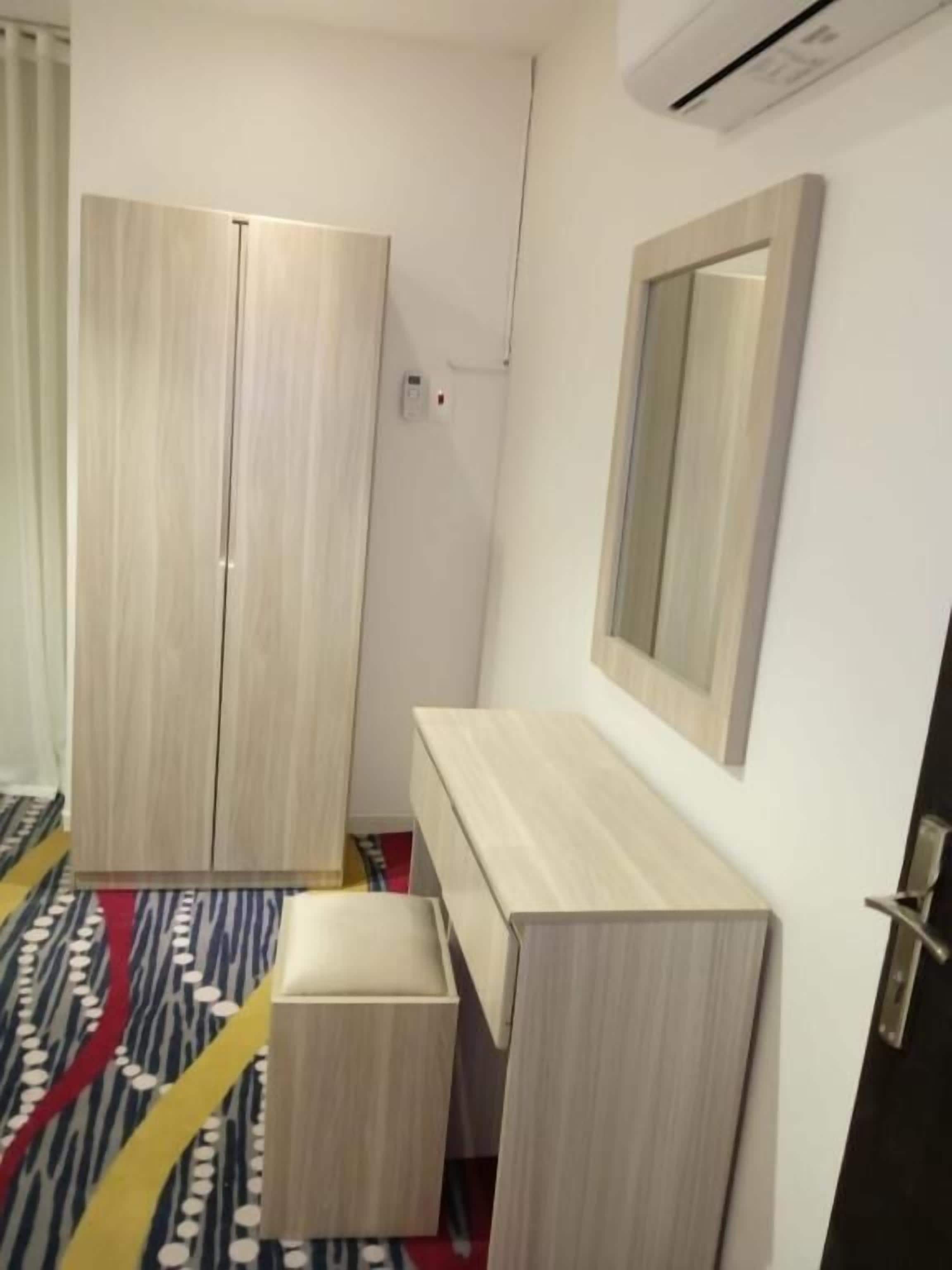 Una habitación de hotel con armario, mesita de noche, espejo y alfombra estampada.