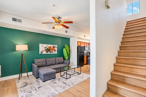 A living room with a sofa, coffee table, floor lamp, and a ceiling fan.