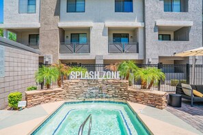 Une piscine bordée d’un mur en pierre et entourée de palmiers, le tout adossé à un immeuble doté de balcons.