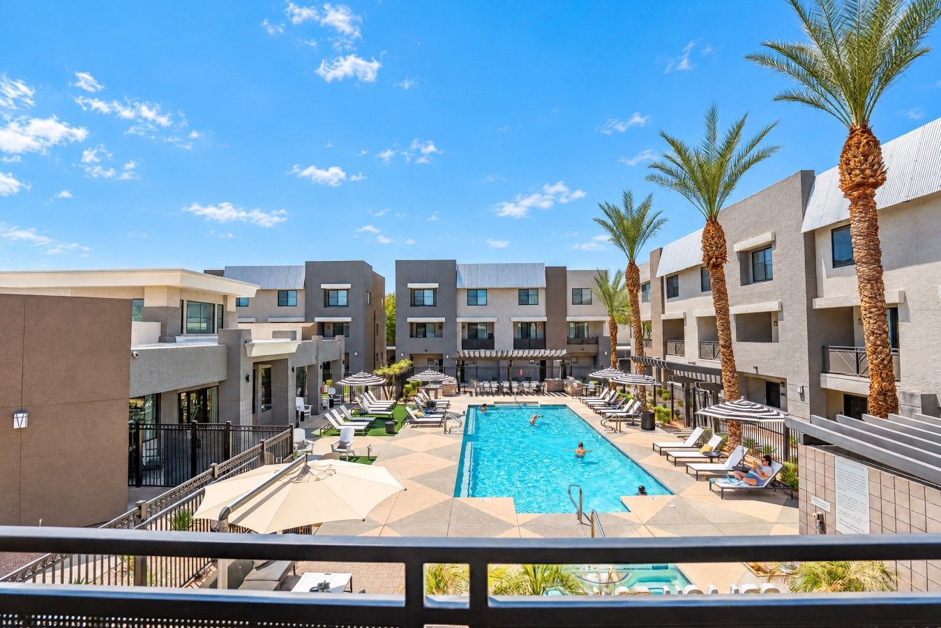 A hotel with a central swimming pool surrounded by lounge chairs and palm trees.