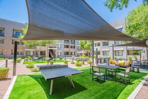 An outdoor seating area with tables and chairs, a ping pong table, and a shaded area.