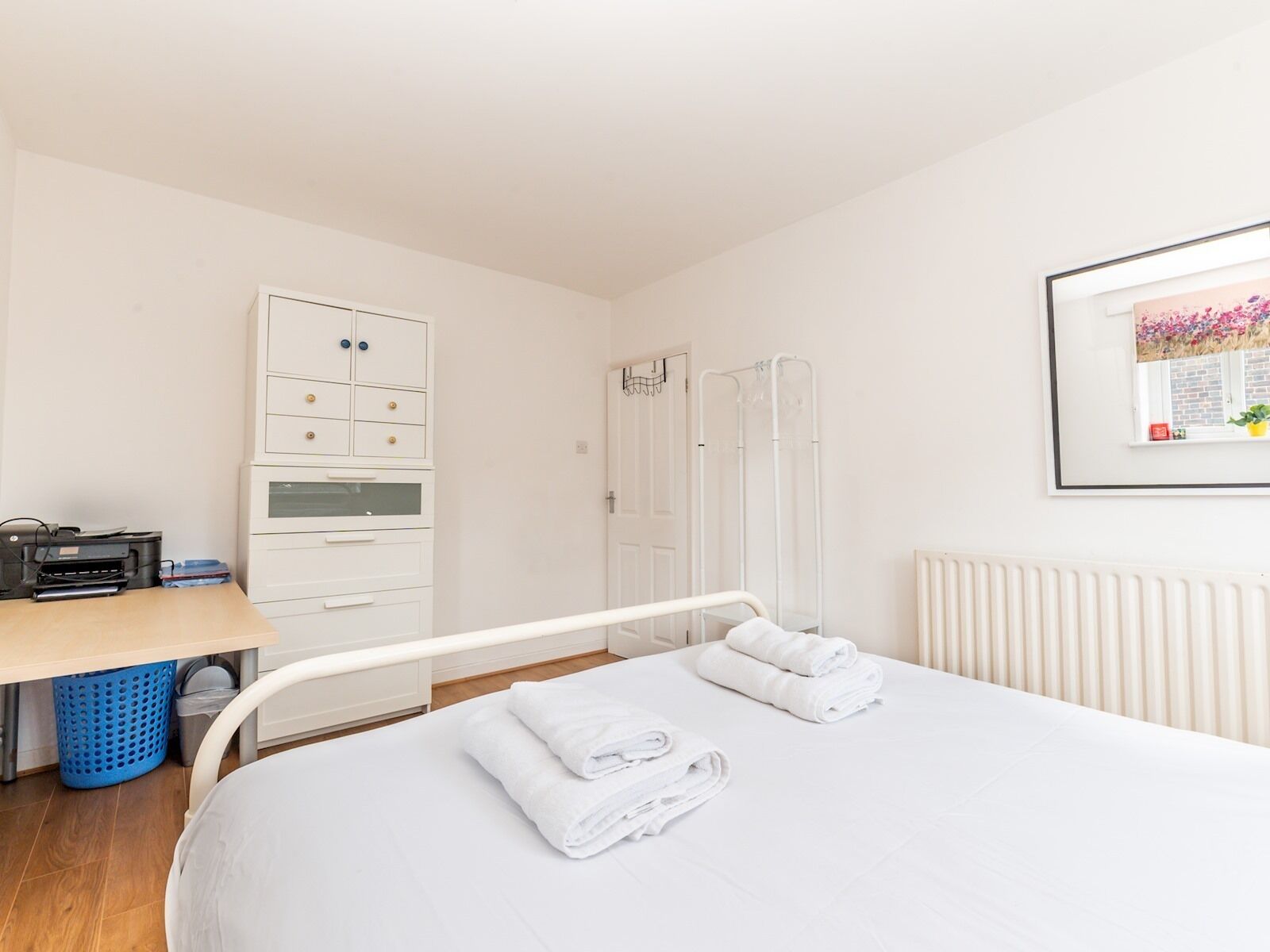Une chambre d’hôtel comprenant un lit, un bureau avec une imprimante, une armoire et un radiateur.