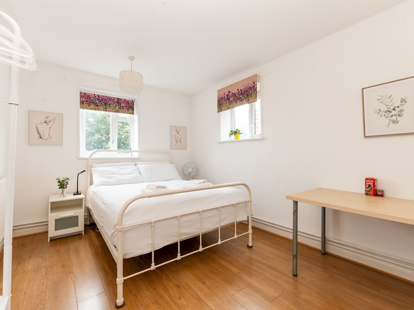 A bedroom with a bed, bedside tables, a desk, and artwork on the walls.