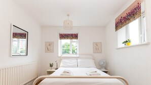 Un dormitorio con cama, mesitas de noche, radiador, ventana con vistas y obras de arte en las paredes.
