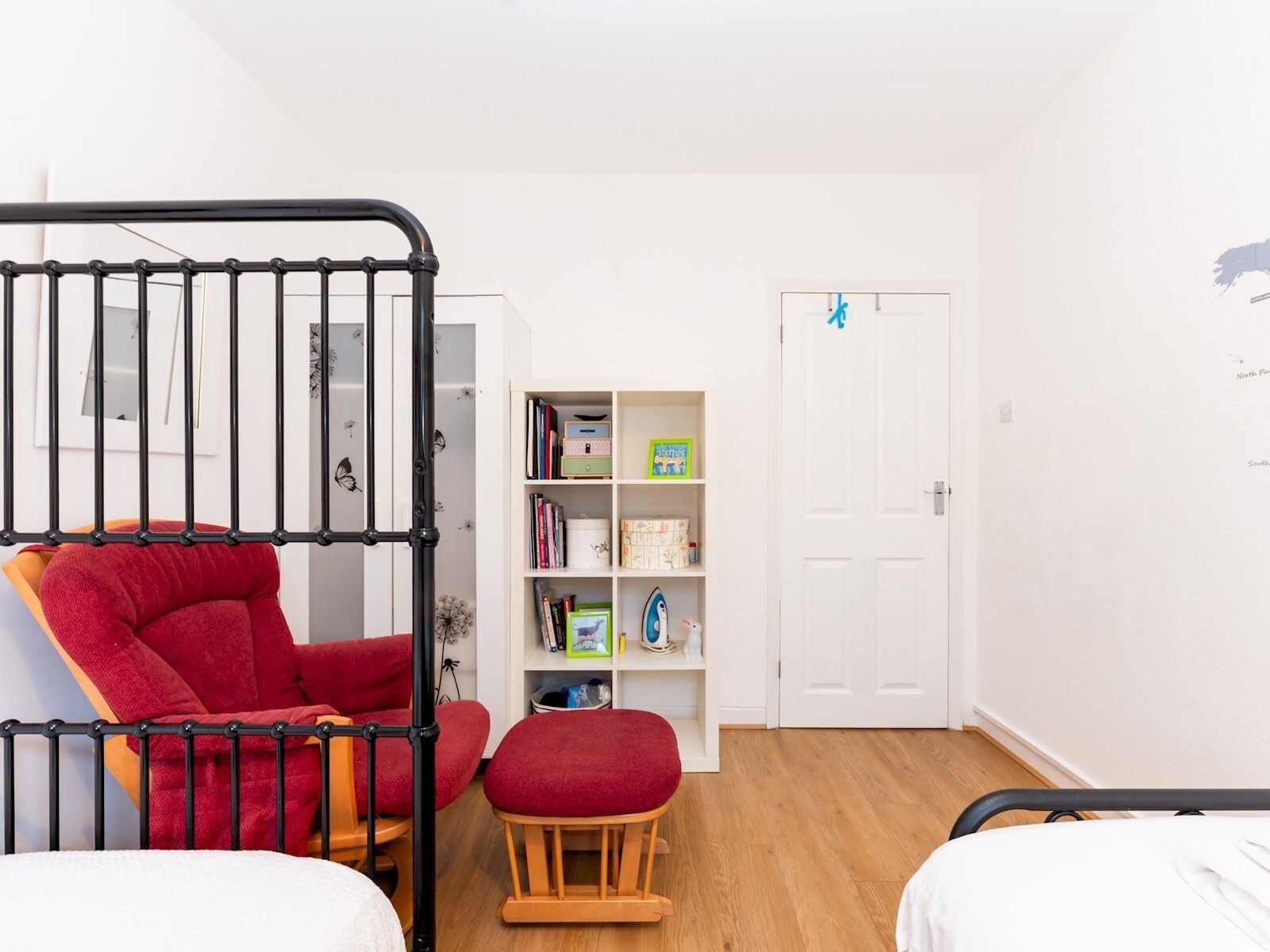 Quarto infantil com beliches, uma cadeira vermelha, um banquinho de madeira e uma estante de livros e brinquedos.