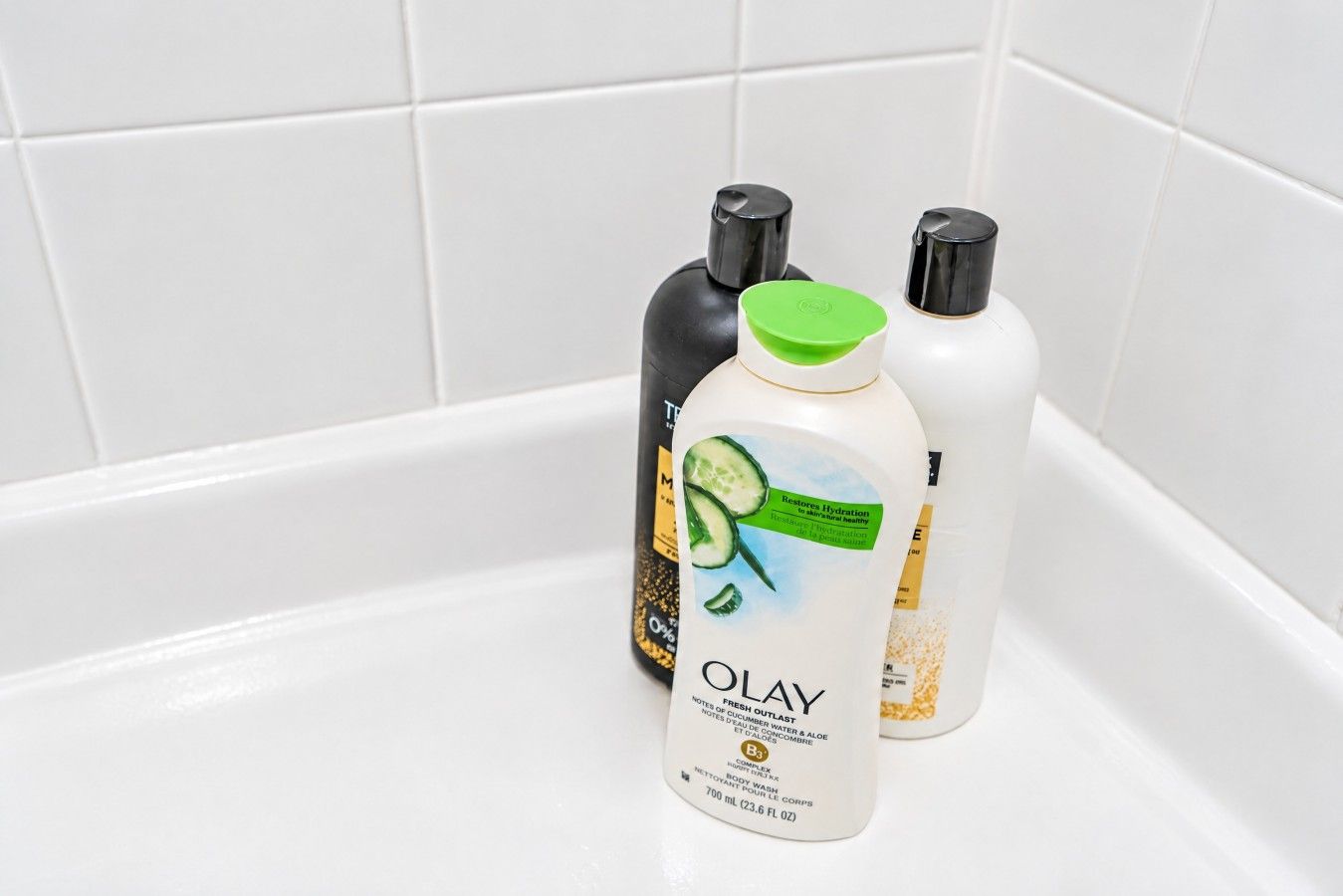 A bathroom with a white bathtub containing three bottles of Olay body wash.