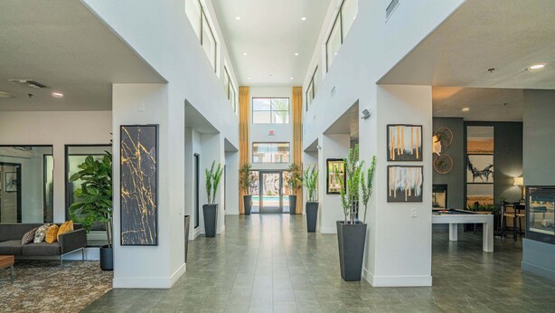 A spacious lobby with a high ceiling, a central staircase, and a view of the building's entrance. - Chic Modern Stay, Pool, W/D, Gym, Walk to Westgate (Glendale)