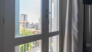 A room with a large window offering a view of urban buildings and greenery. - Italianway Easy - Giambellino 67 A (Milano)