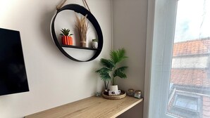 A corner of a room with a wooden desk, a round mirror, and a potted plant.
