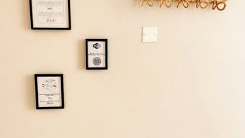 A wall with four framed items: a no-smoking sign, a framed certificate, a framed certificate with a logo, and a wall-mounted hook.