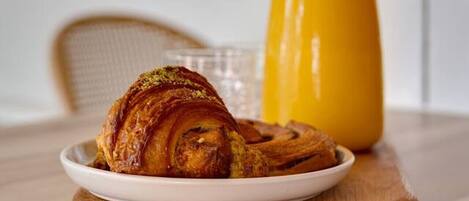 A breakfast setting with a croissant on a wooden board, a glass of orange juice, and a coffee maker.