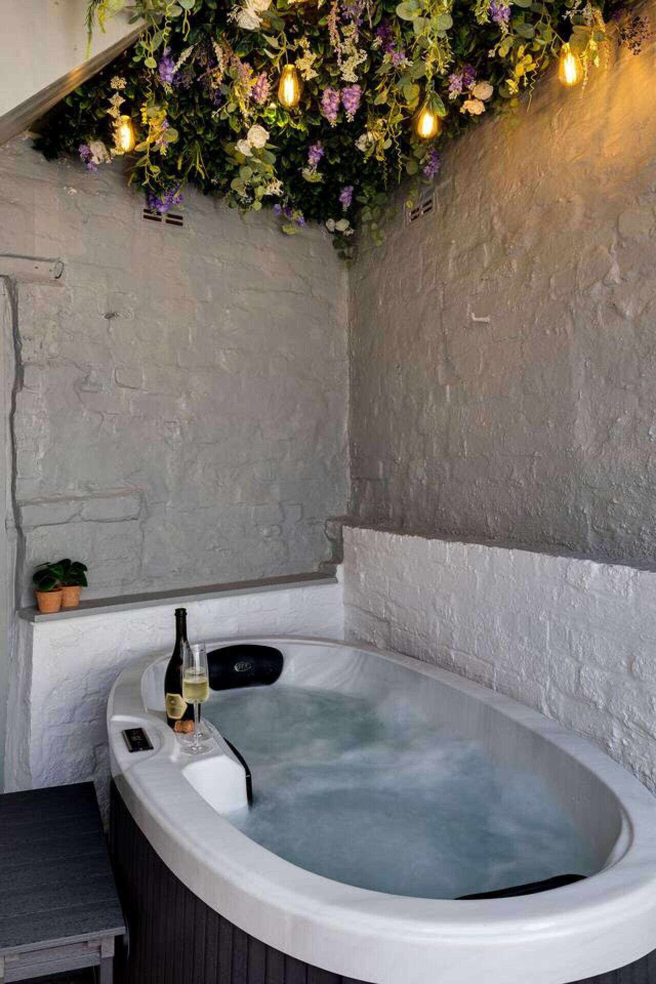 Un espace spa comprenant un bain à remous, une plante en pot et un verre à vin posé sur une table.