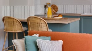 A modern kitchen with a central island, two wicker chairs, a sofa with cushions, and a hanging light fixture.