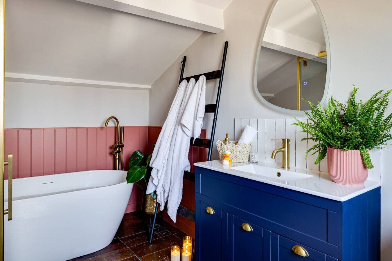 A bathroom with a white bathtub, a blue vanity, a mirror, and a potted plant.