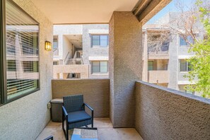 A balcony with a chair and a trash can, overlooking a building with multiple windows and balconies. - Contemporary Condo at Westgate | Pool, Gym & W/D (Glendale)