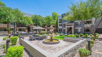 A courtyard with outdoor seating, a central fountain, and modern buildings in the background.