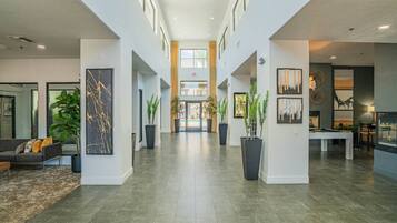 A spacious lobby with a high ceiling, a pool table, and potted plants.