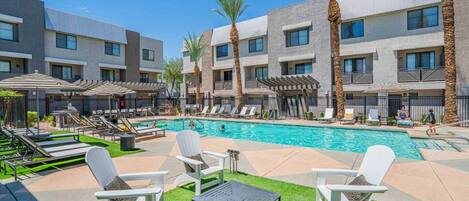 A poolside area with lounge chairs, a pool, and a building with multiple balconies.