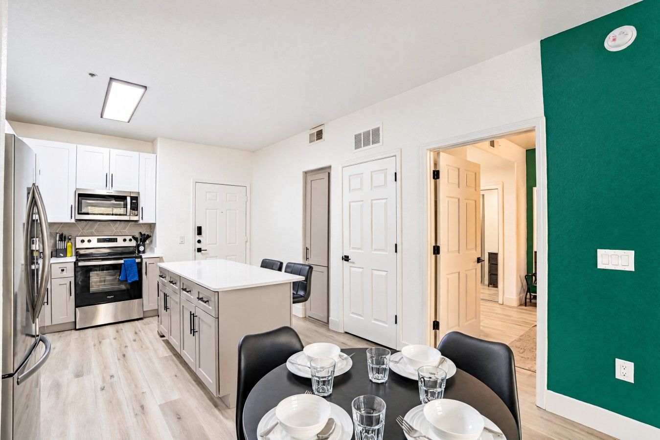 A modern kitchen with stainless steel appliances, a dining area with a table set for two, and a green accent wall.
