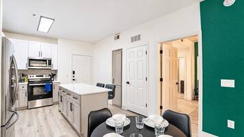 A modern kitchen with stainless steel appliances, a dining area with a table set for two, and a green accent wall.