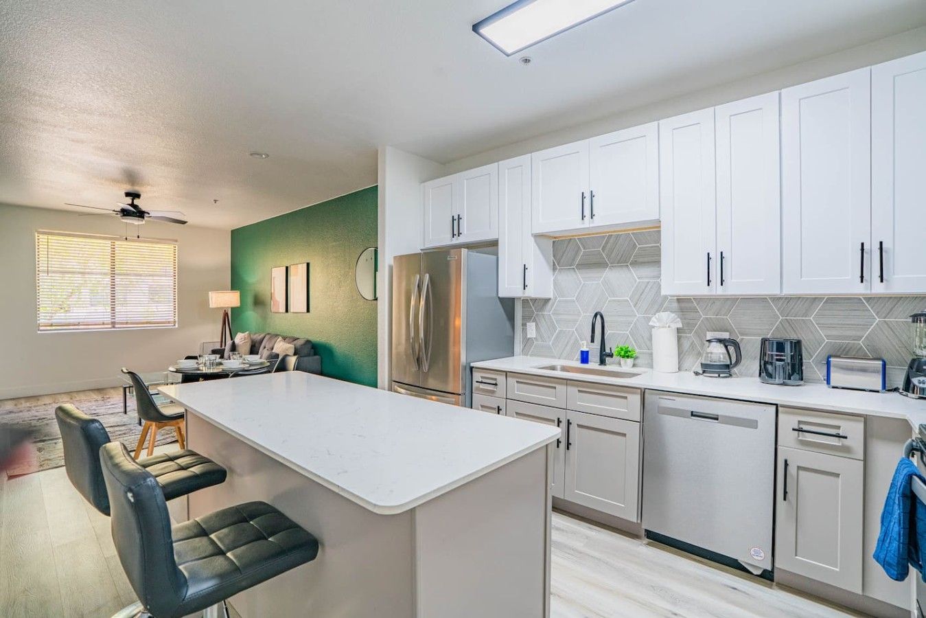 A modern kitchen with white cabinets, a central island, and a dining area with a sofa and chairs.