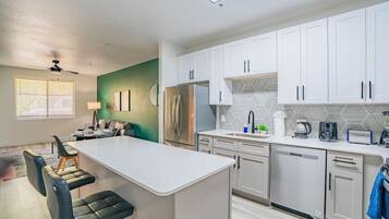 A modern kitchen with white cabinets, a central island, and a dining area with a sofa and chairs.