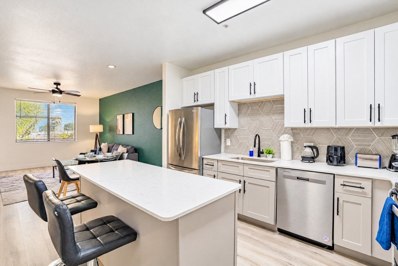 A modern kitchen with white cabinets, a central island, and a dining area with a sofa and chairs.